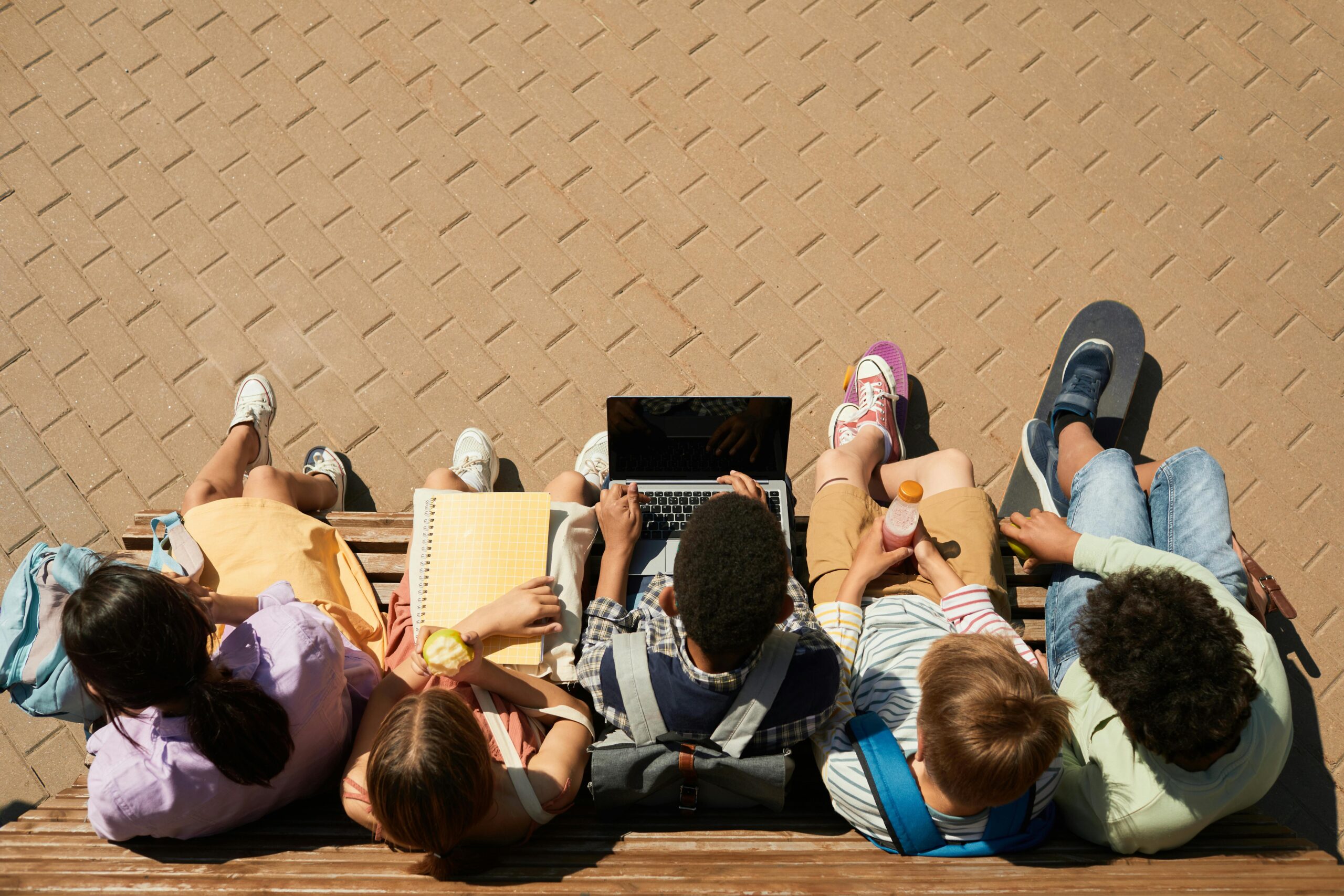 Birds eye view of five schoolchildren sitting on wooden bench