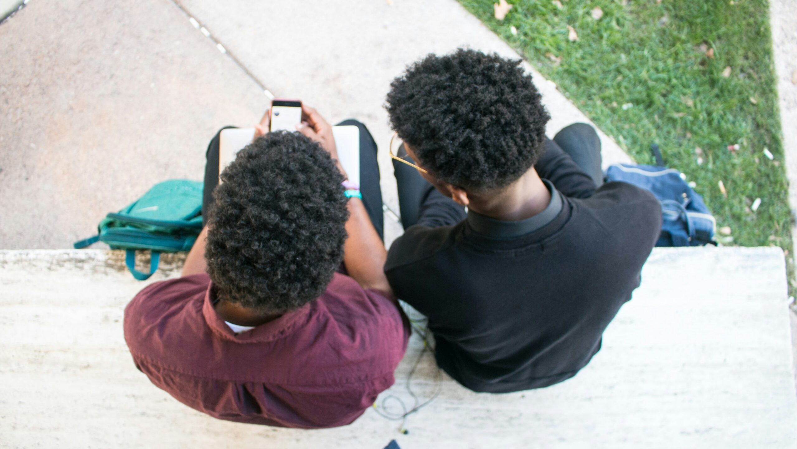 Overhead view of two Black teens sitting and looking at one's phone
